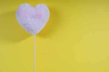 pink fluffy heart on a stick, with the edge of the frame on a yellow background, festive mood, loving atmosphere, place for an inscription