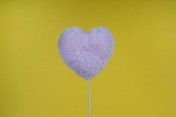 pink fluffy heart on a stick, with the edge of the frame on a yellow background, festive mood, loving atmosphere, place for an inscription