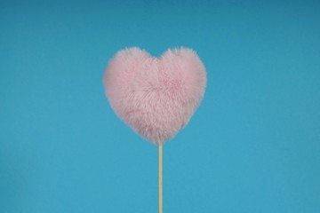 pink fluffy heart on a stick, in the middle of the frame on a blue background, festive mood, love atmosphere