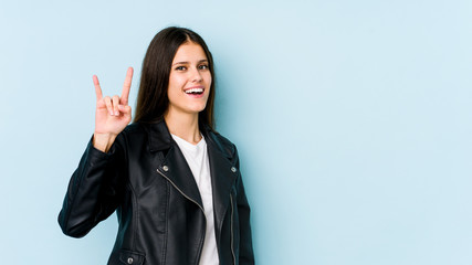 Young caucasian woman isolated on blue background showing a horns gesture as a revolution concept.