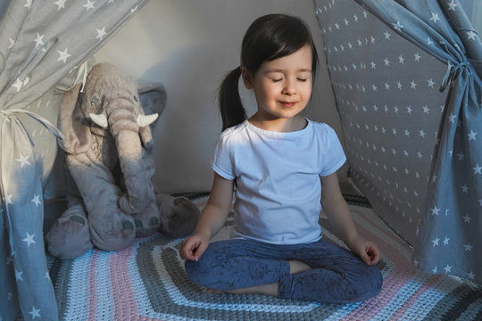 The child does yoga. Little girl is sitting in lotus position. Children's yoga for spinal health.