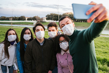 Group of teenagers friends taking a selfie at park wearing medical masks to protect - Conceptual...