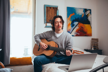 young man playing acoustic guitar in his room