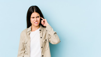 Young caucasian woman isolated on blue background covering ears with hands.