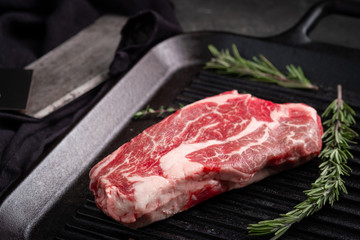One Perfect raw steak Chuck roll of beef on a black pan with a grill with rosemary