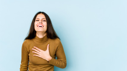 Young caucasian woman isolated on blue background laughs out loudly keeping hand on chest.