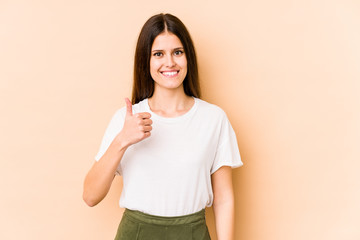 Young caucasian woman isolated on beige background smiling and raising thumb up