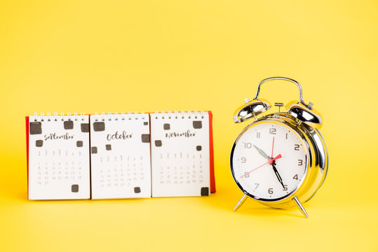 Alarm clock and calendar with autumnal months on yellow background
