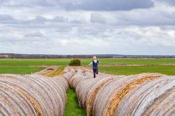 Child running on long row of round hay bales on overcast day. Childhood on the farm, country life.