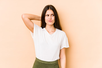 Young caucasian woman isolated on beige background touching back of head, thinking and making a choice.