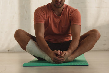 Cropped view of man with broken leg stretching on fitness mat on floor