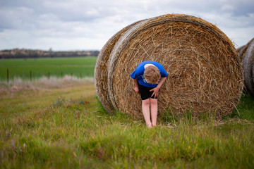 Child bending down near long row of round hay bales on a farm at winter time