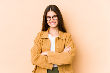 Young caucasian woman isolated on beige background who feels confident, crossing arms with determination.