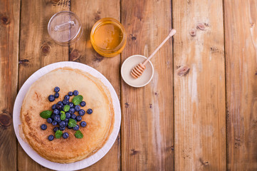 Pancakes with blueberries and honey on a plate, on wooden roofing. Traditional pastries for the Russian festival of Maslenitsa. free space for text. Above. Banner