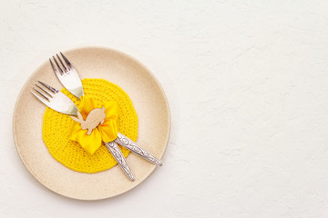 Easter table setting on textured white putty background. Spring holiday card template. Cutlery, knitted napkin, flower