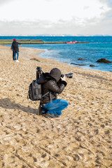 Photographer traveler with a camera and a backpack on the beach in spring when it is still cold, takes pictures sea