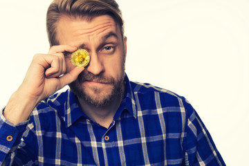 Portrait of a winking man holds a coin bitcoin in front of his eyes