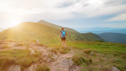 Fototapeta premium Early morning in the mountains. Young man runs on a trail in the mountains. Background illustrating a healthy lifestyle.