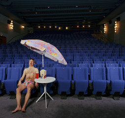 man alone wearing shorts and sunglasses in cinema with parasol, scared, crazy funny