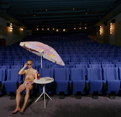 man alone wearing shorts and sunglasses in cinema with parasol smiling, crazy funny