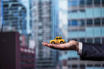 The hand of a businessman in a suit holding a toy yellow taxi car on the background of office...