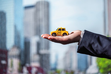 The hand of a businessman in a suit holding a toy yellow taxi car on the background of office...
