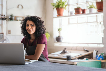 Fototapeta na wymiar Smiling woman working on a laptop in her framing shop