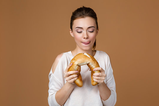 Portrait Of Beautiful Young Woman Eating Delicious Bread Baguette On Studio Yellow Background. Girl With Fresh Fragrant Long Loaf