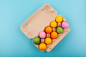 Colorful handmade Easter eggs. Top view of an open gray box. Isolated on a blue background. Preparing for Easter.