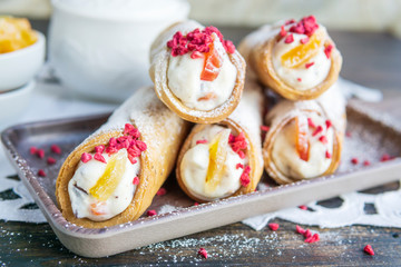 Sicilian cannoli  deep fried pastry tubes on wooden board with a sweet ricotta cream and colorful dried candied fruits. Homemade Italian dessert on rustic table, white napkin near window. Copy space.