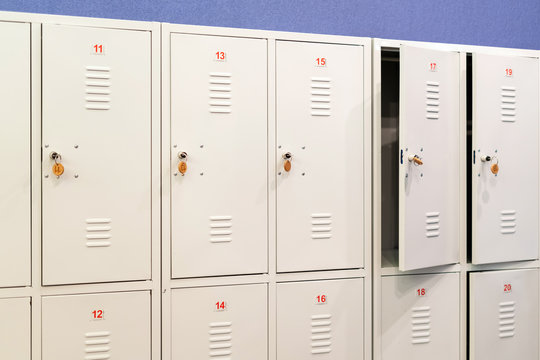 A row of grey metal school lockers with keys in the doors. Storage locker room in corridor of educational institution
