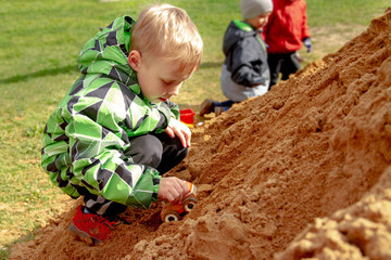 Boy rolls a toy car in the sand. Games on the Playground.