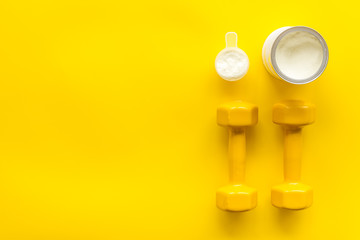 Sport diet. Protein shake near dumbbells on yellow background top-down flat lay copy space