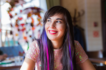 Young stylish trendy woman with multi-coloured strand in hair sits in cafe