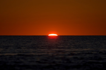The beginning of a sunrise over the ocean with the sun just peeking over the calm water horizon.