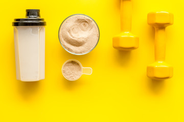 Sport diet. Protein shake near dumbbells on yellow background top-down flat lay copy space