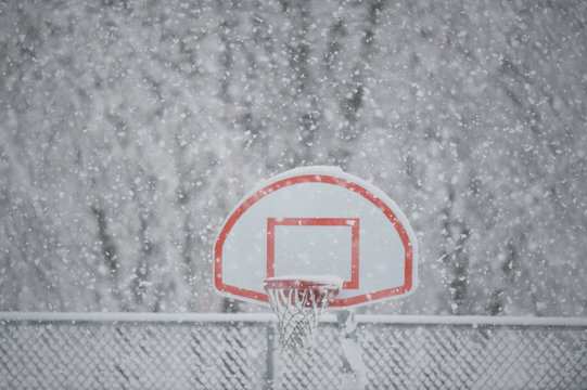 Heavy snow falls on a basketball hoop on a cold winter day.