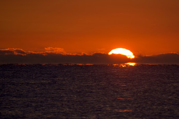 The sun rises over the ocean with clods on the horizon and the water looks dark.