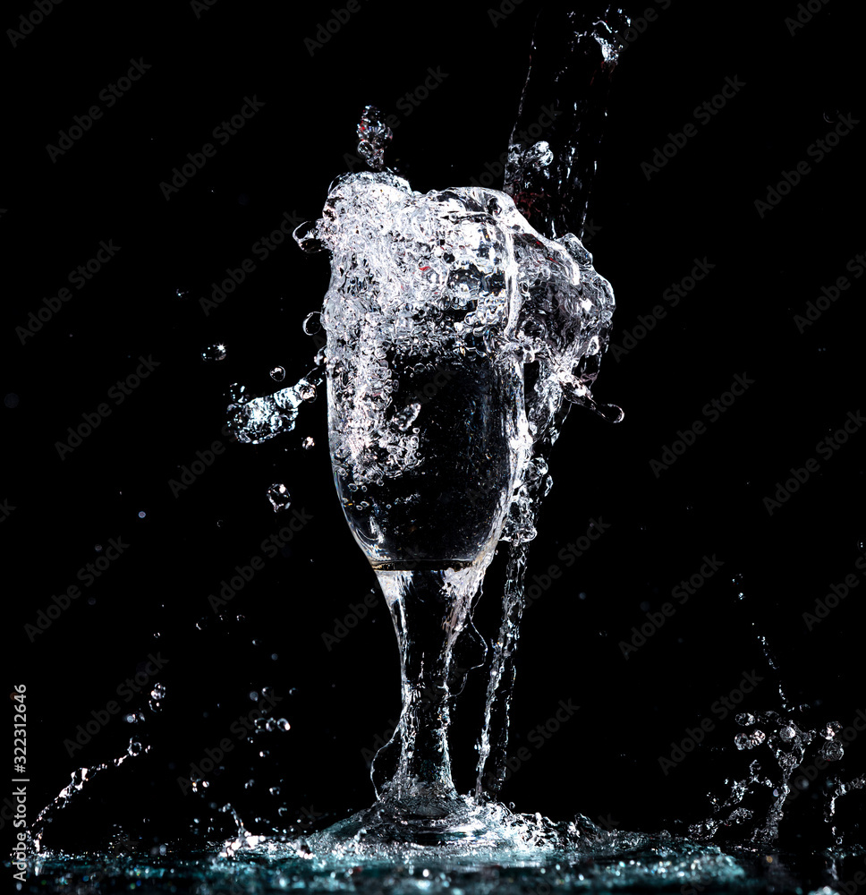 Wall mural Water with splashes in a glass on a black background