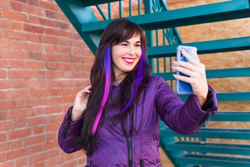 Technologies, urban and people concept - Pretty girl with long coloured hair takes a selfie on the rooftop