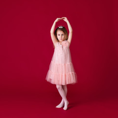 Beautiful little girl princess dancing in luxury pink and silver dress isolated on red background. Funny face, different emotions