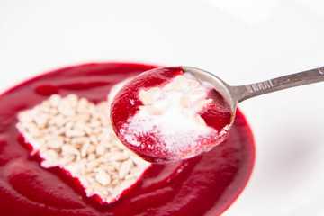 Beetroot cream soup decorated with a heart made of yoghurt and sunflower seeds eaten with a vintage spoon