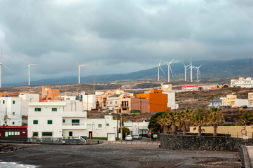 Obraz premium Small coastal town of Las eras at sunset. Concrete houses that look like boxes. In the distance, you can see wind turbines-alternative energy sources. 