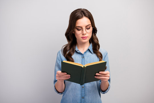 Photo of pretty concentrated business lady hold book hands addicted reader book worm not smiling wear specs casual jeans denim shirt isolated grey color background
