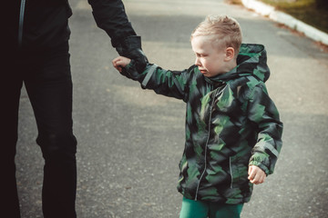 A man leads by the hand of a crying child. The boy doesn't want to go to kindergarten.