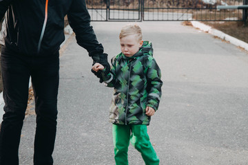 A father leads a crying child by the hand. The boy wants his mother.