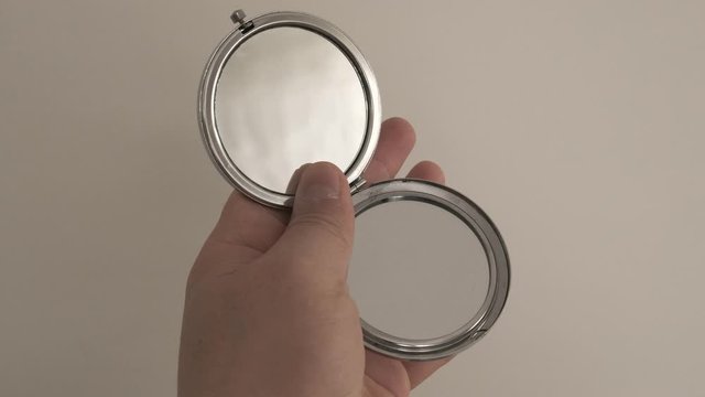 pocket mirror in the hand of a person on white ground,