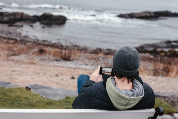 Young man sitting on the bench and chatting in smartphone.