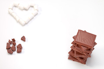 A concept of loving chocolate, a pile of milk chocolate and crunches of chocolate and a marshmallow in a shape of heart isolated, passion, desire, ardour to a bar of chocolate