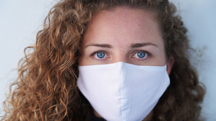 beautiful blond-haired curly girl in a medical mask on a light background. Serious blue-eyed girl...